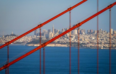 The San Francisco skyline rests behind the geometric patterns of the Golden Gate Bridge's cables.